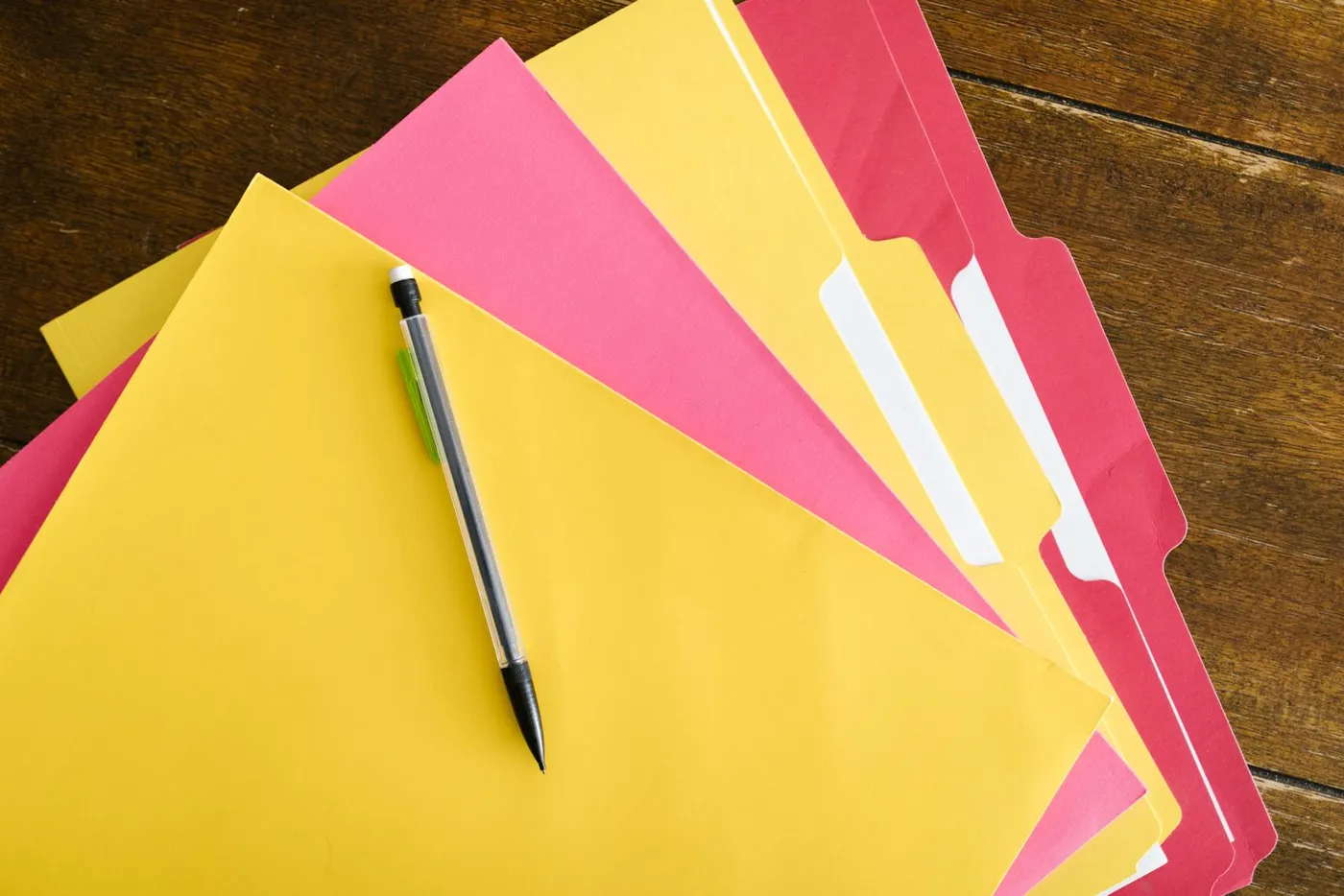 Colorful folders and a pen fanned out on a wooden table.