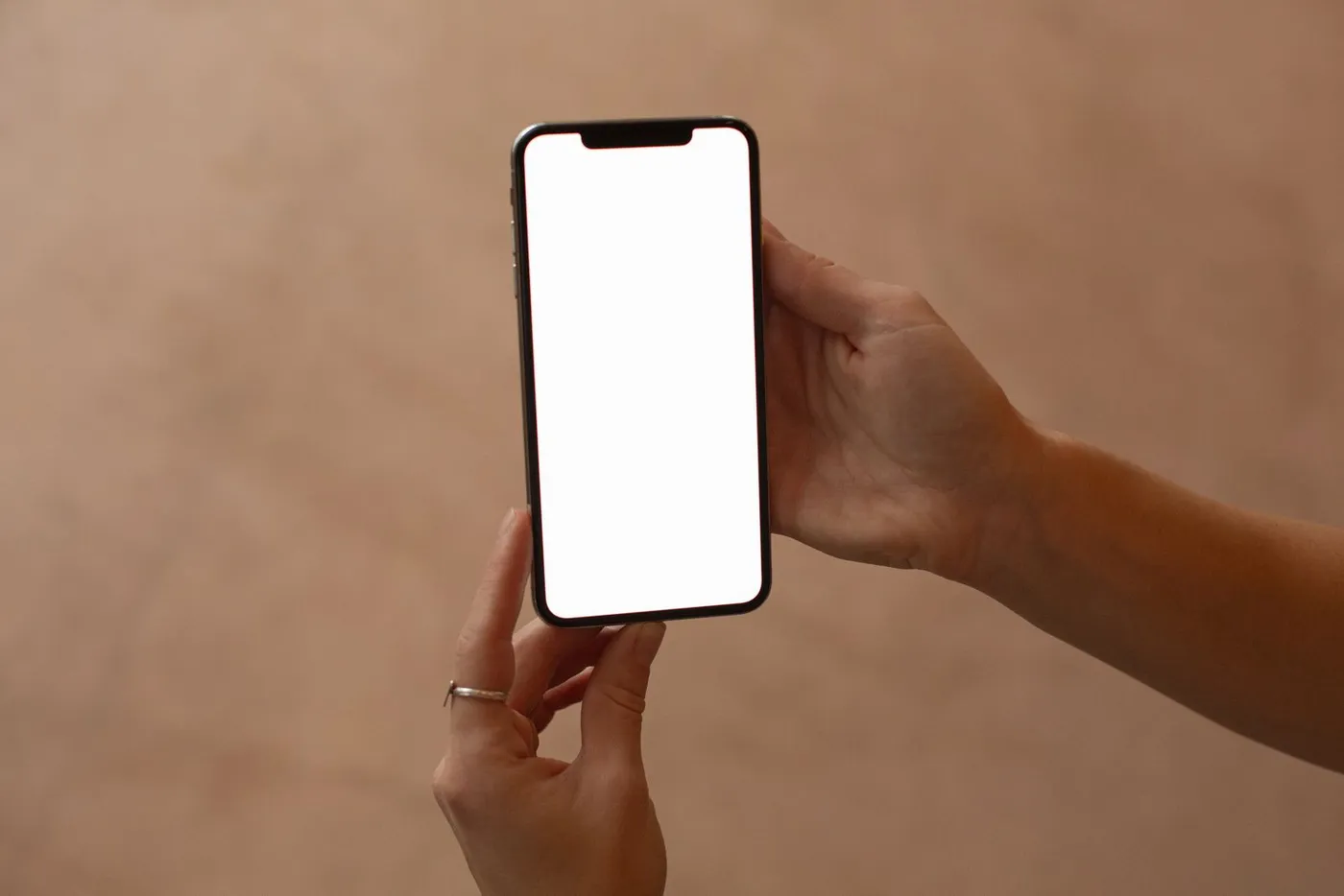 Two hands holding a black smartphone with a blank white screen, against a warm-toned background.