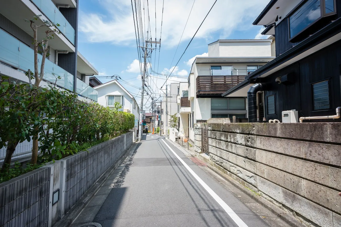 A quiet residential street in a Japanese suburb with detached houses, overhead power lines and a clear blue sky.