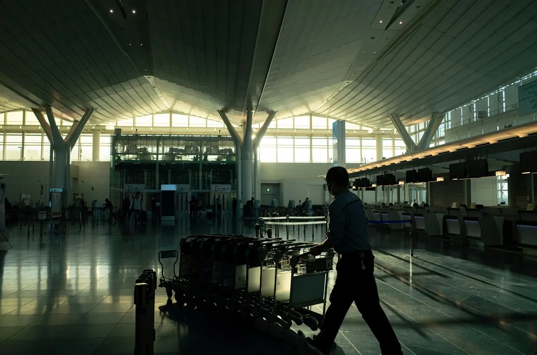 A person pushing a line of luggage carts across a bright airport departure hall.