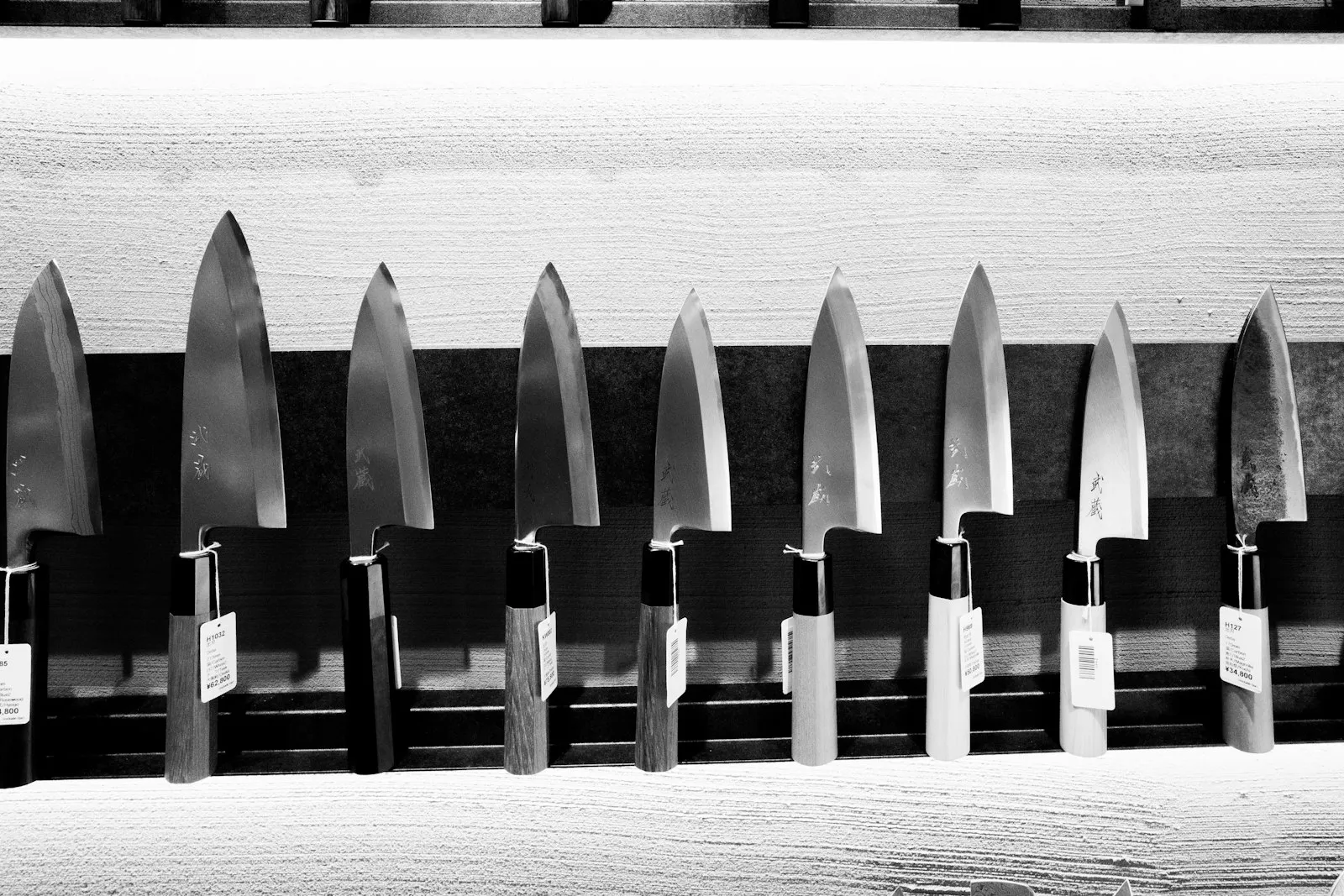 A row of Japanese kitchen knives lined up on a display rack.
