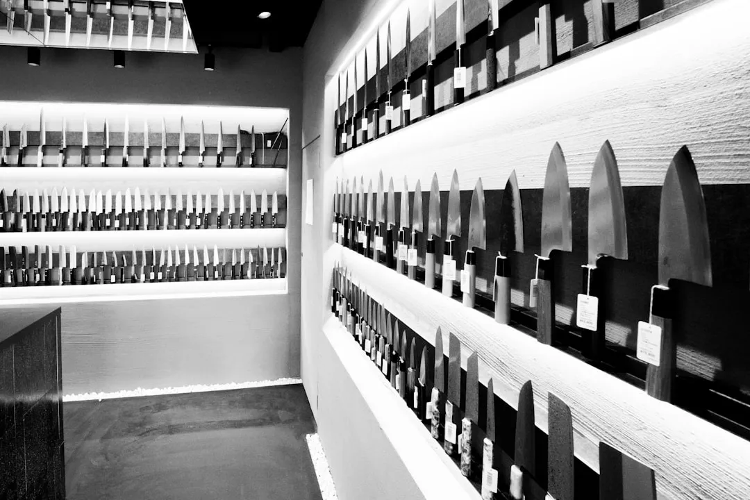 The interior of a knife shop with rows of blades and price tags on lit wall shelves.
