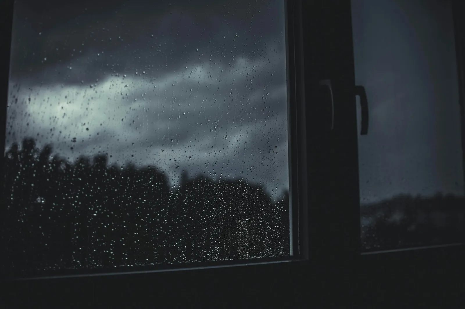 Raindrops on a window at night, with a door handle visible through the glass.