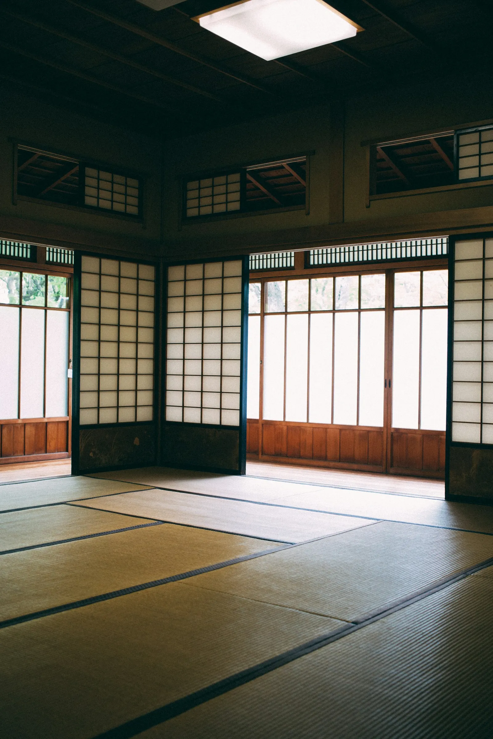 An empty tatami-mat room with sliding paper doors and windows on two sides.