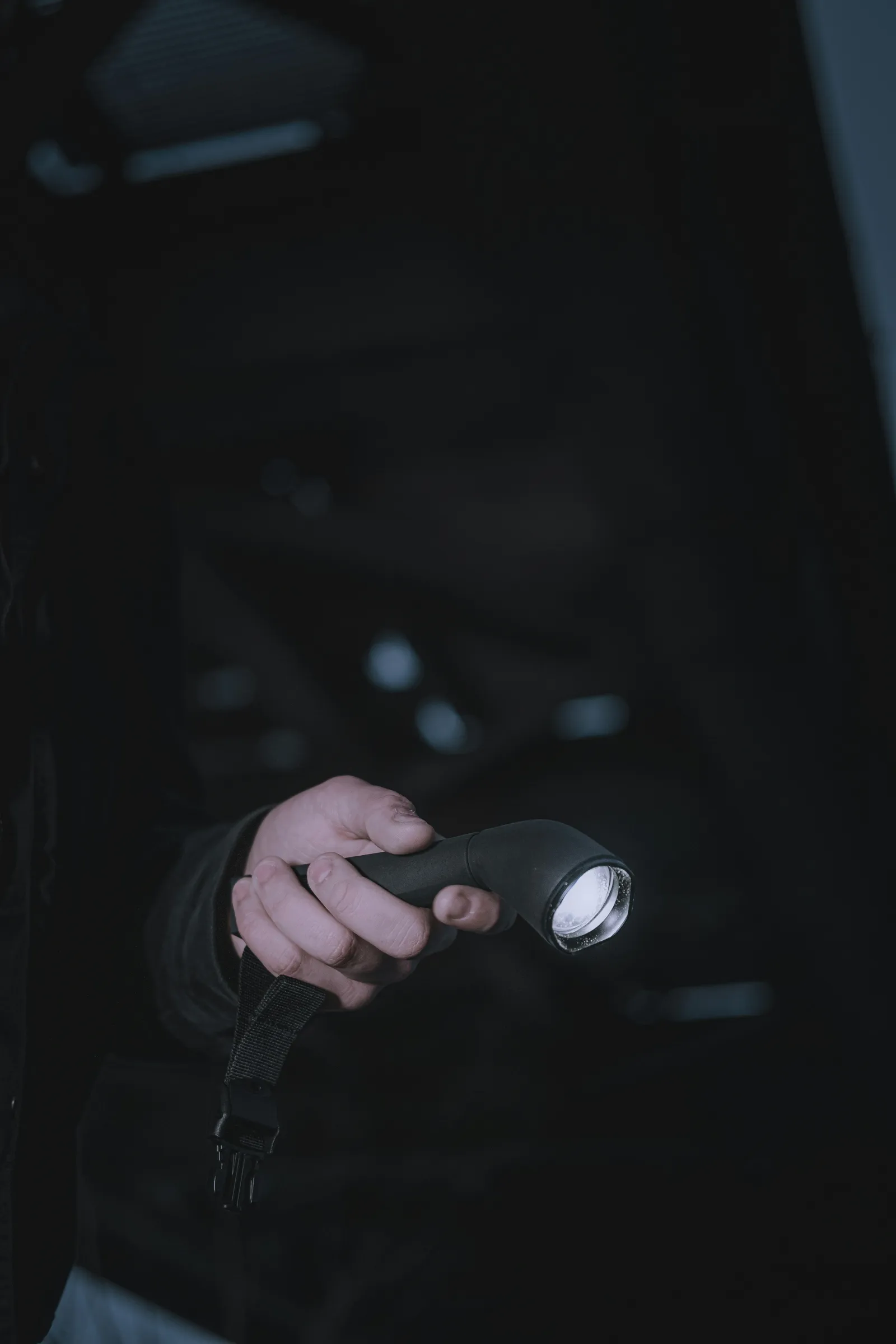 A hand holding a flashlight that is switched on, in the dark.