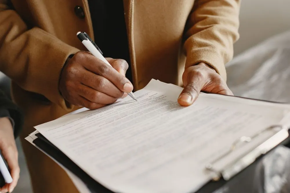 Two hands filling in a printed form held on a clipboard.