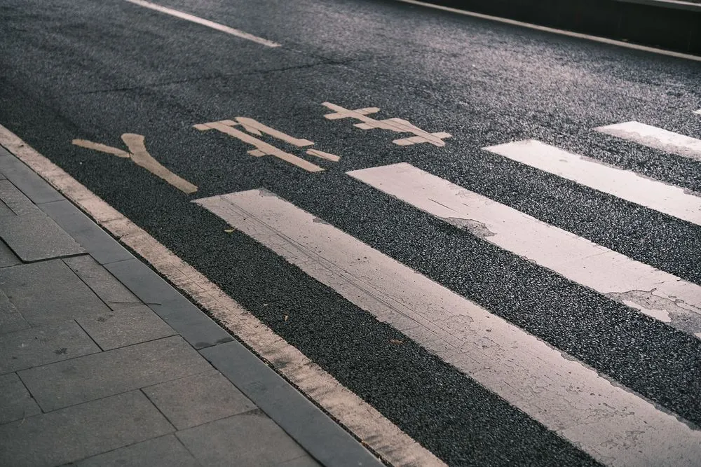 A pedestrian crossing painted across an asphalt road next to a paved sidewalk.