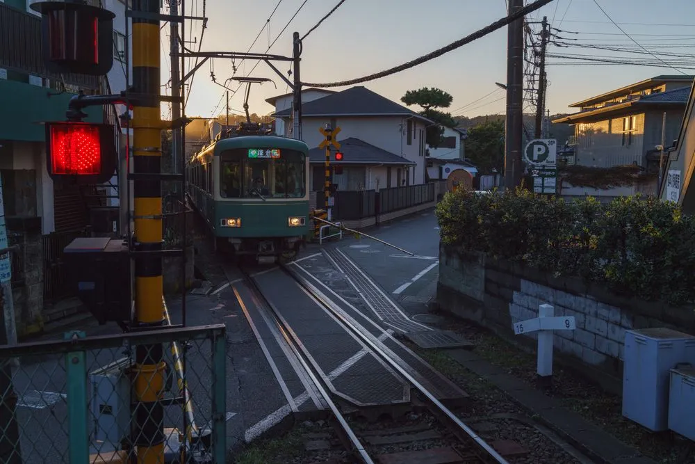 A railway crossing in a residential street at dusk with a train approaching and the warning light lit.