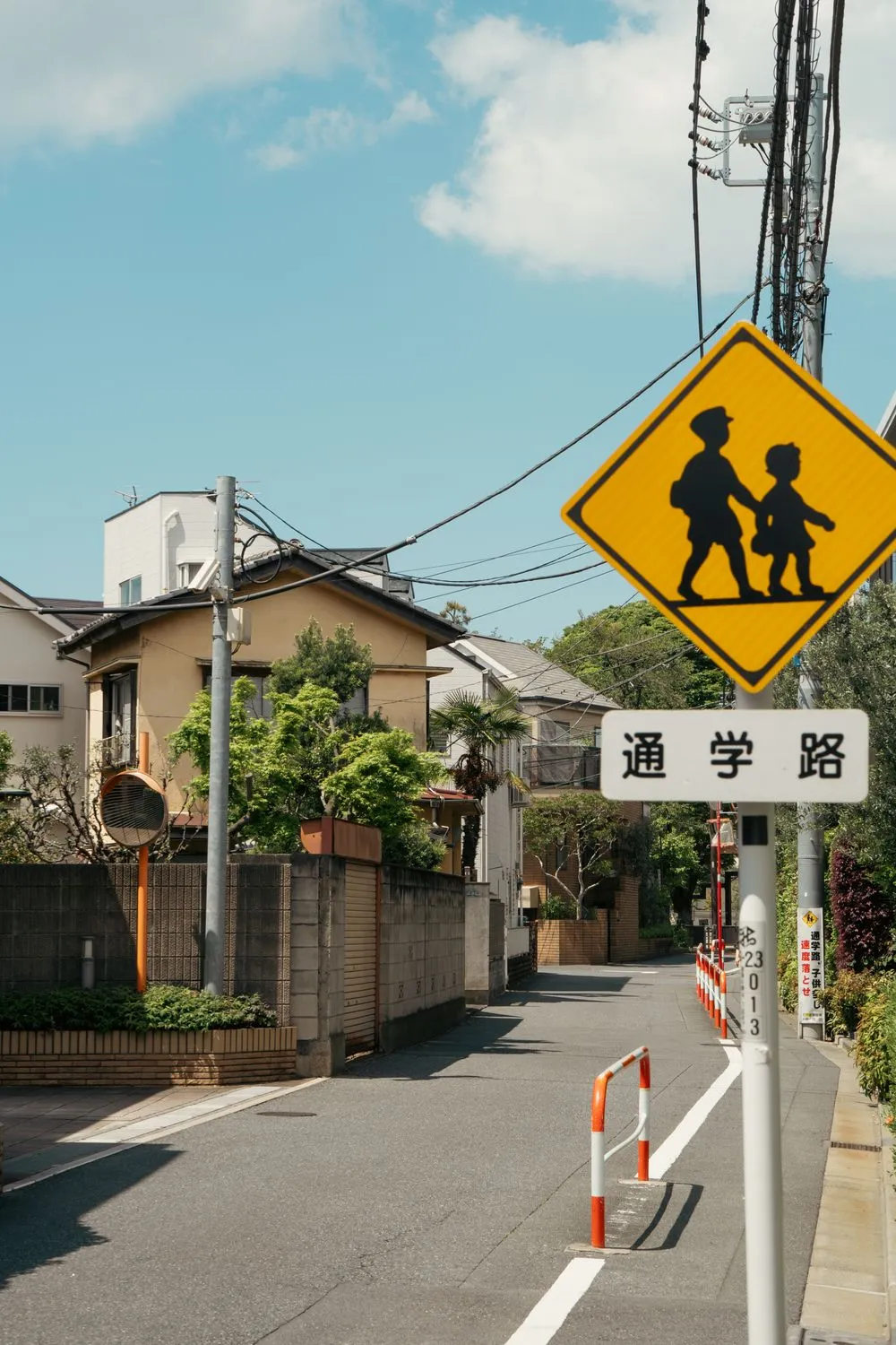 A Japanese residential street with a yellow pedestrian warning sign and a school route sign.