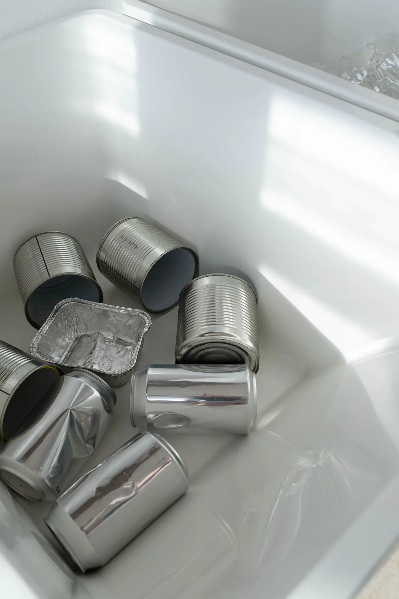 Rinsed steel and aluminum cans and a foil tray inside a clean white container.