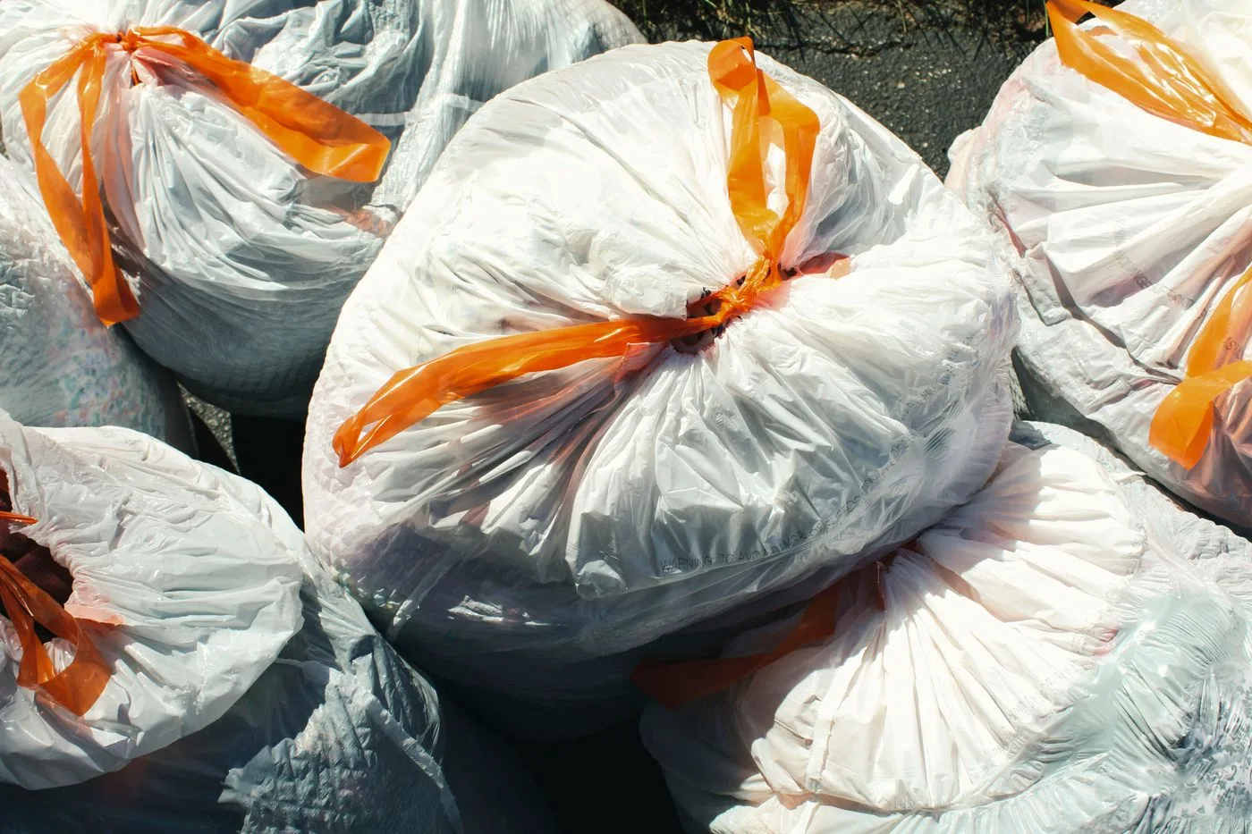 Household waste bags in translucent white plastic, closed with orange ties, waiting at the curb.