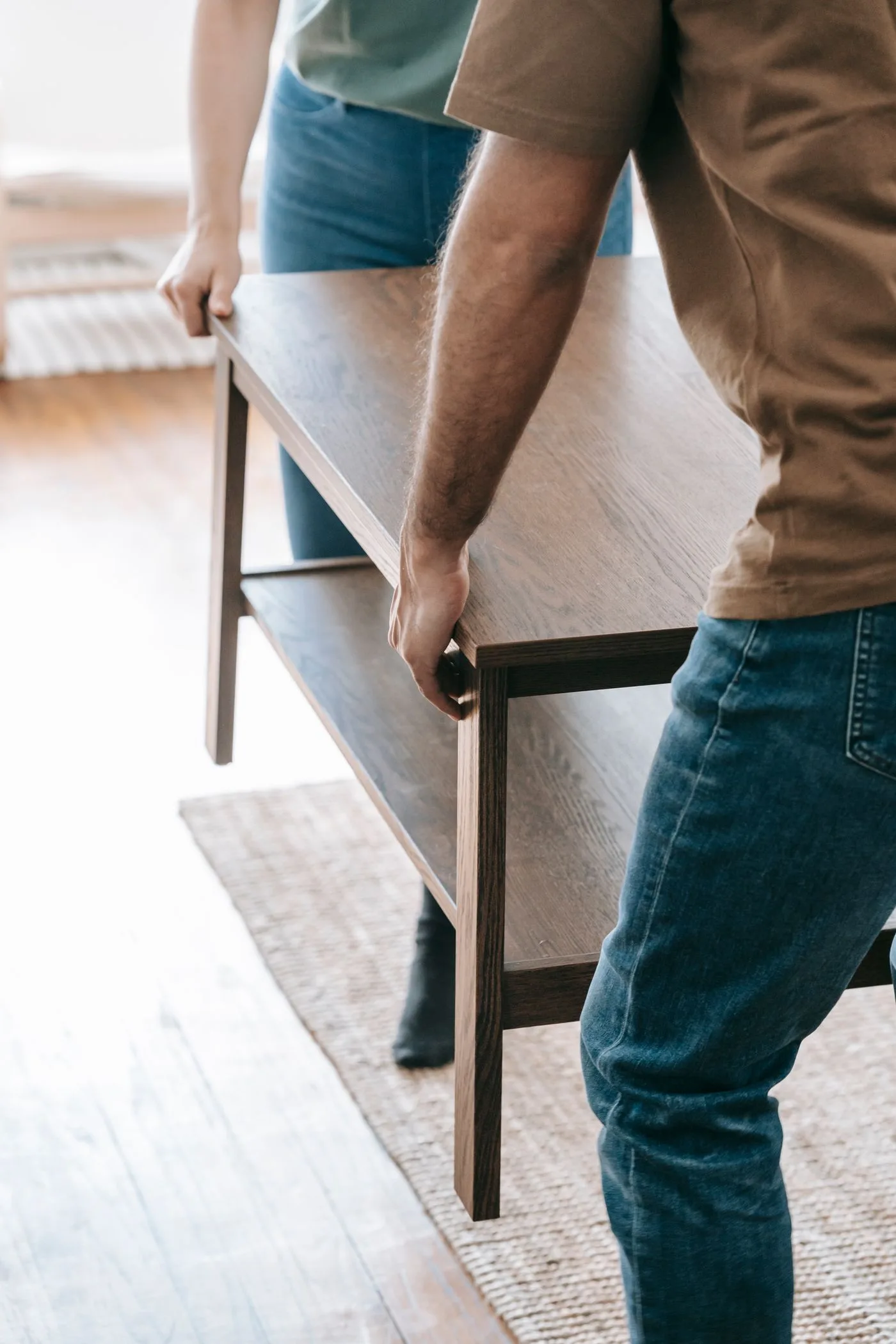 Two people carrying a wooden table together across a room.