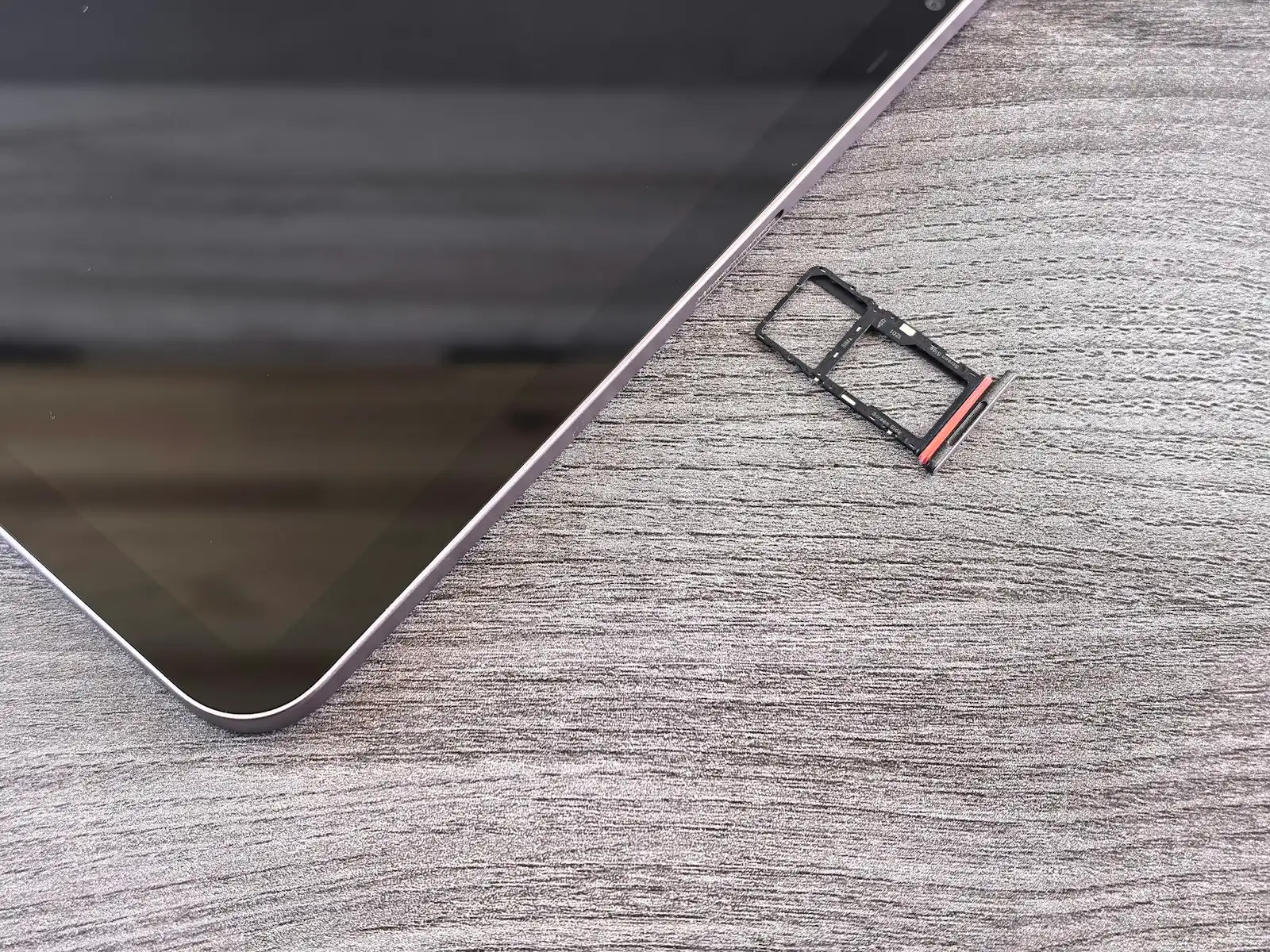 A SIM card tray removed and resting on a desk beside a smartphone.