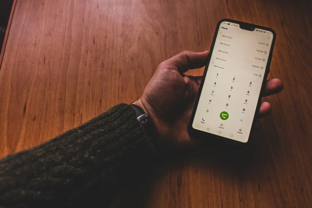 A hand holding a smartphone showing the phone dial pad and a green call button.