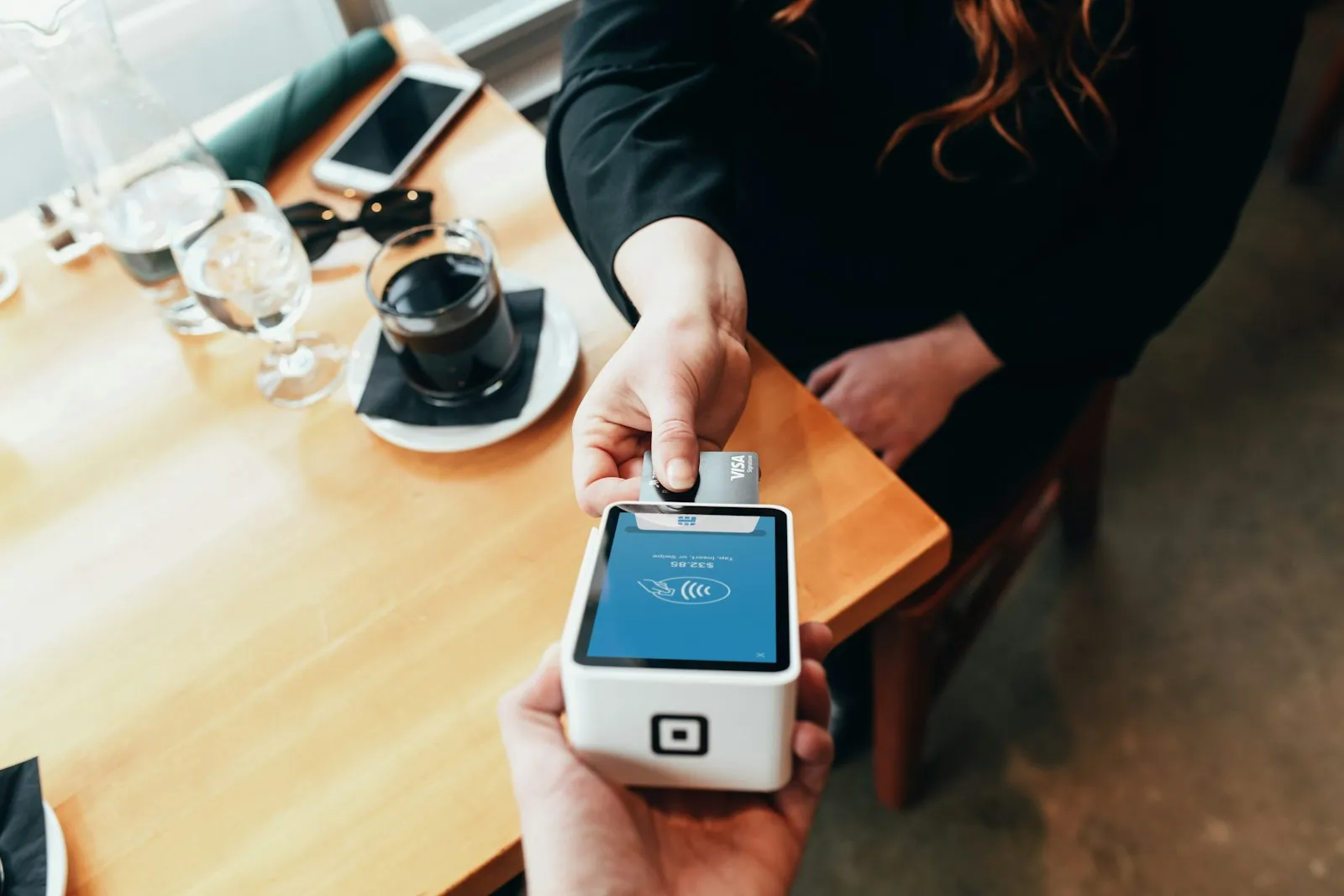 A hand holding a portable card payment terminal at a table.