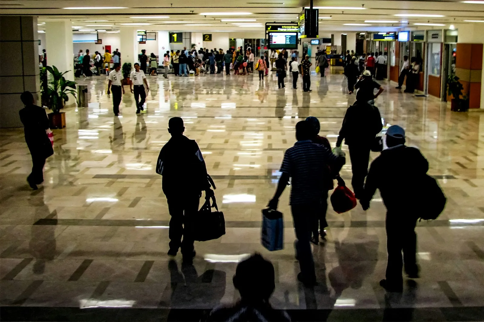 Travelers walking with luggage through a crowded airport terminal.