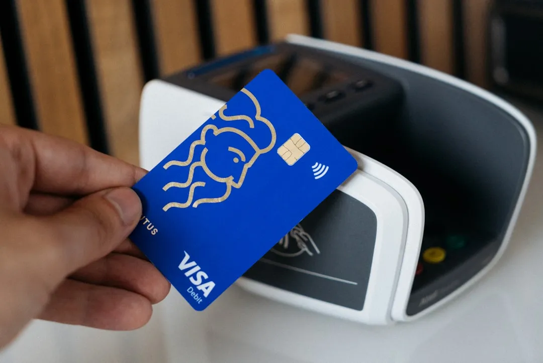 A hand holding a blue chip-and-contactless payment card in front of a card reader.