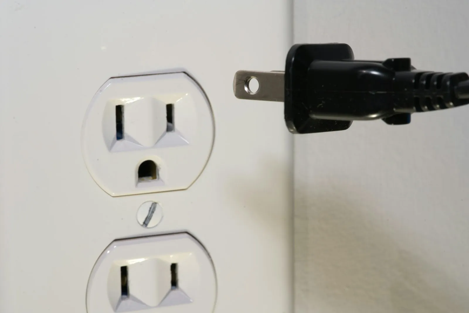 A black power plug in front of a US-style wall outlet.