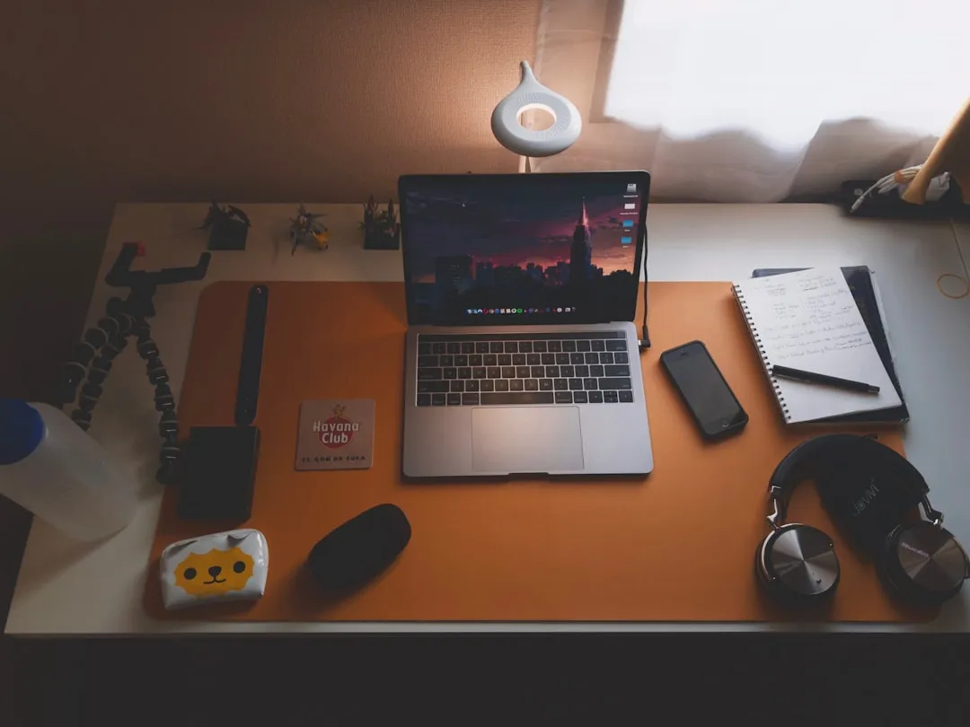 A desk with an open laptop, a smartphone and a notebook with handwritten pages.