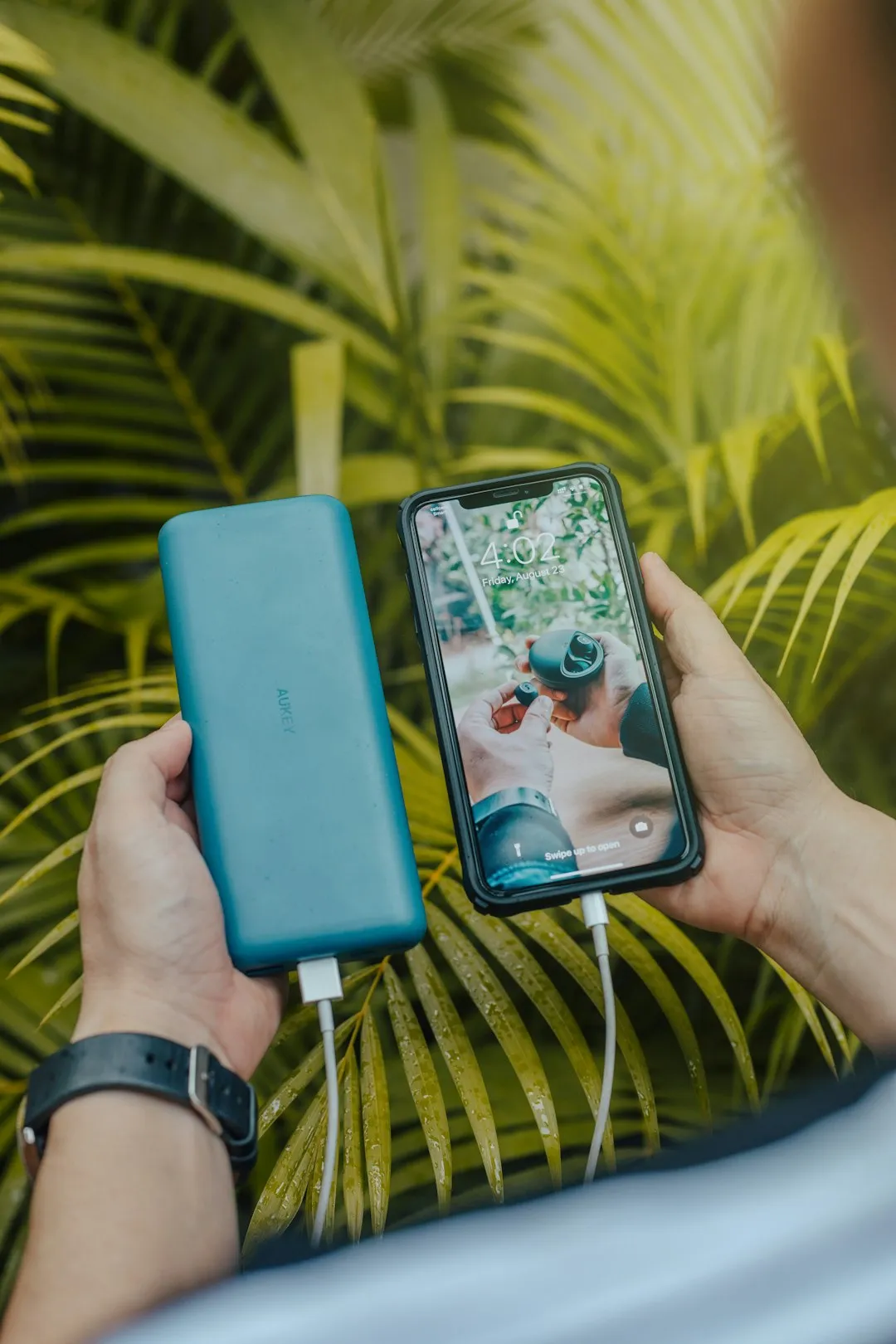 Hands holding a smartphone connected by cable to a portable battery pack.