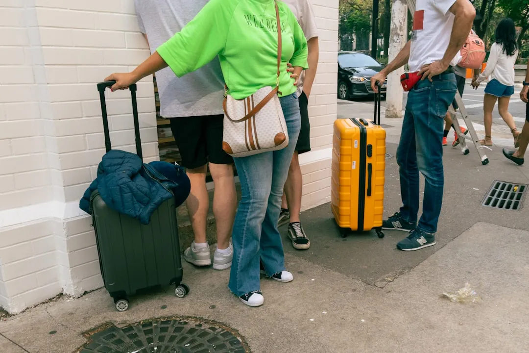 Several people standing together on a pavement with wheeled suitcases.