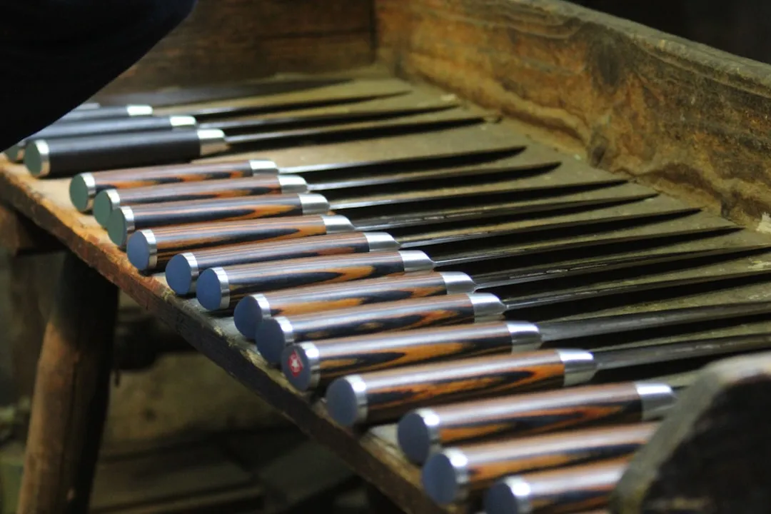Kitchen knives with patterned wooden handles laid out in a row on a workbench.