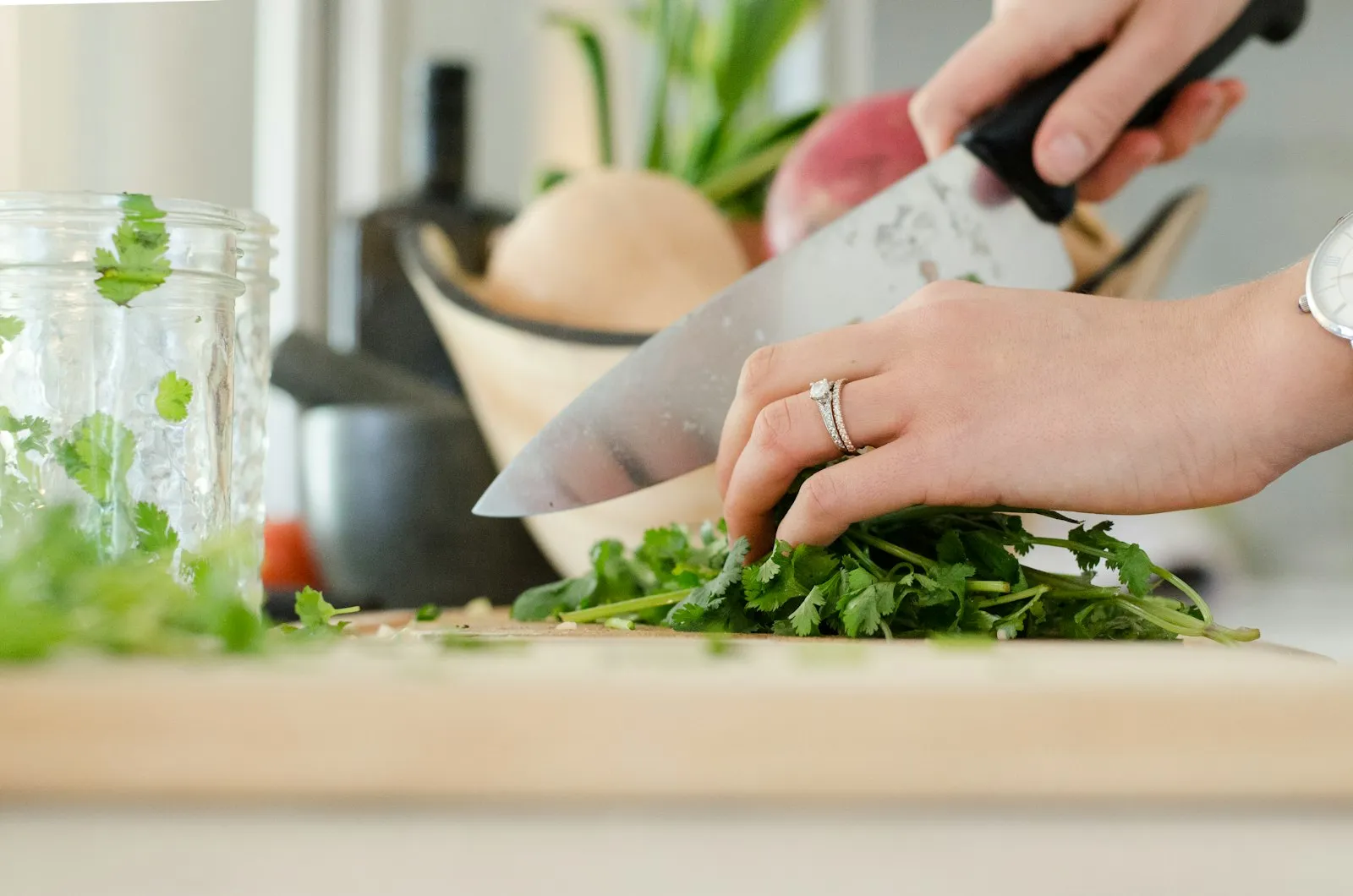 Hands chopping fresh herbs on a wooden board with a kitchen knife.
