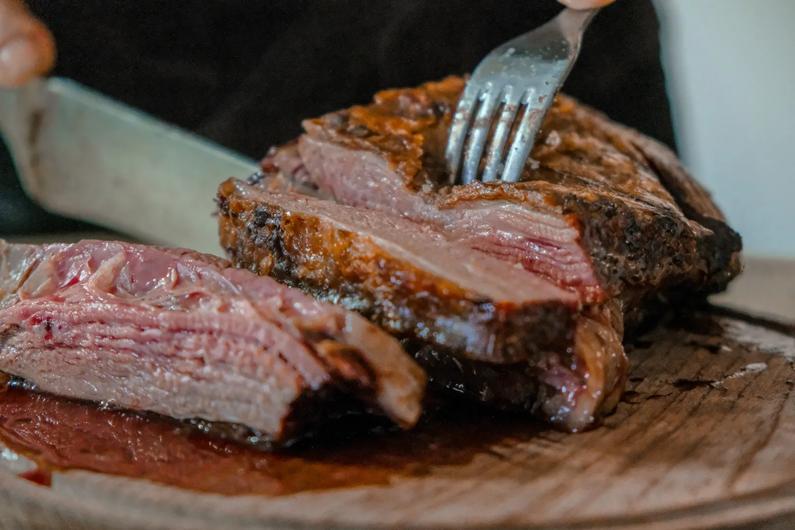 A knife slicing through a cooked cut of meat on a wooden board.