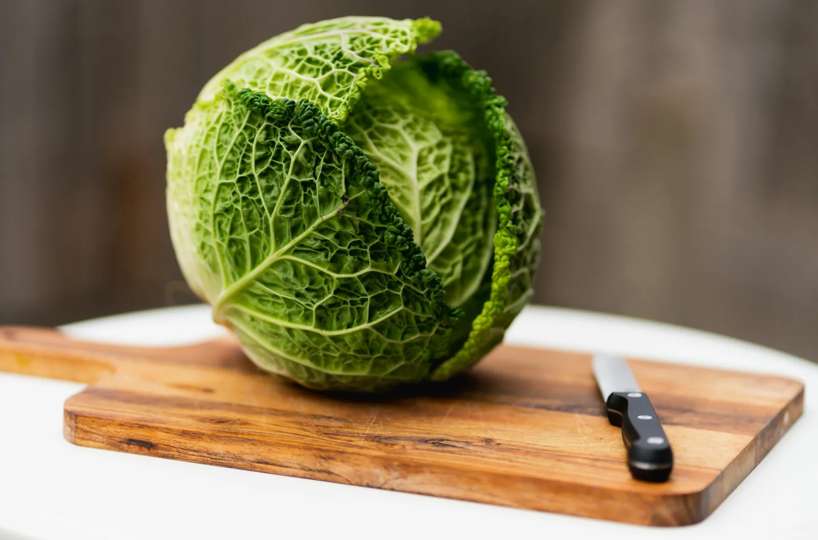 A whole cabbage on a wooden cutting board next to a knife.