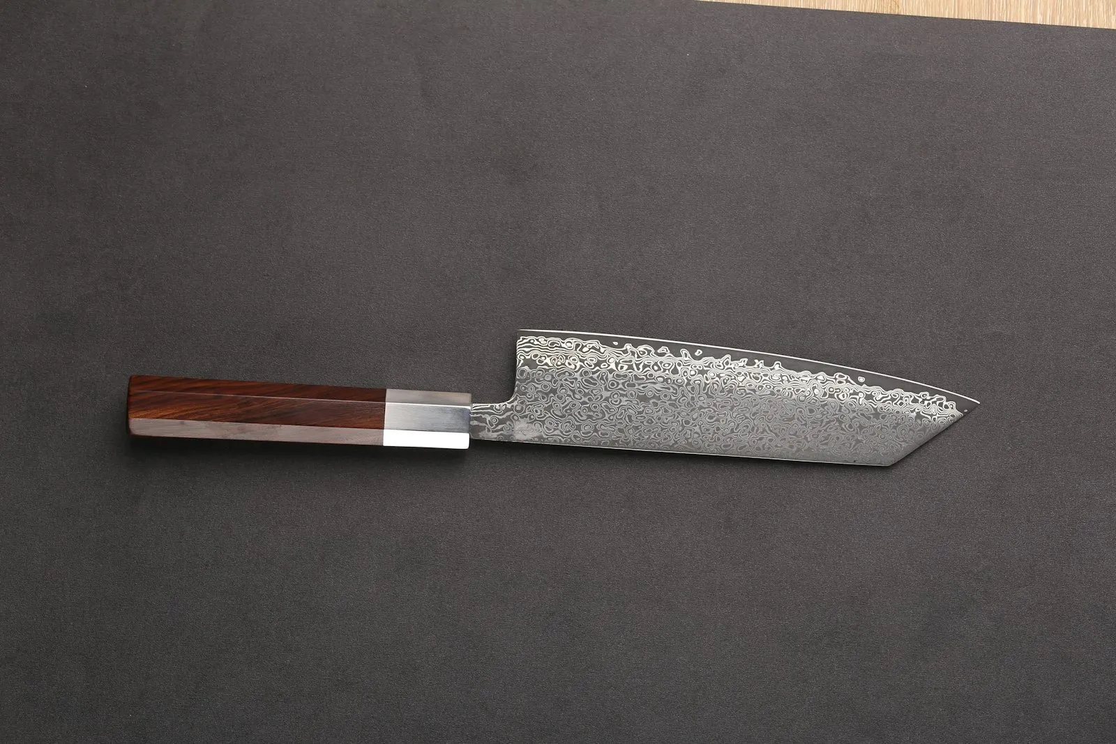 A Japanese kitchen knife with a wooden handle and a squared-off tip on a dark surface.