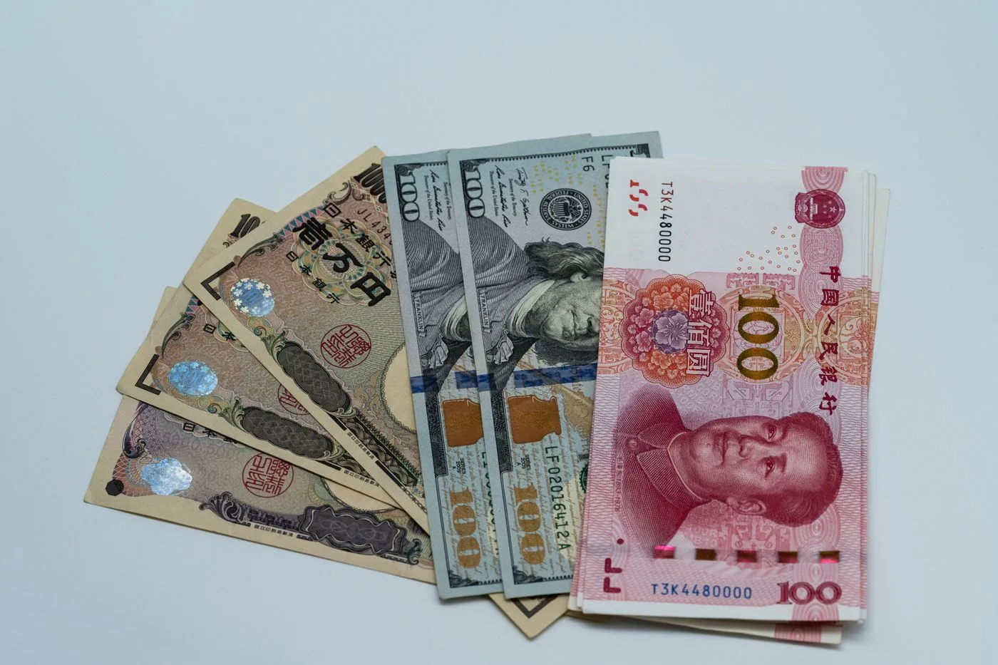 Japanese ten-thousand-yen notes fanned out beside United States dollar bills and a Chinese hundred-yuan note on a pale surface.