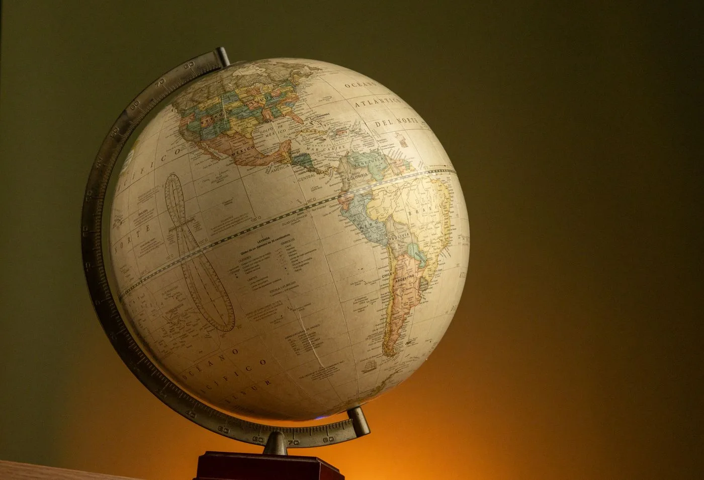 A vintage world globe on a wooden stand, lit from one side against a dark background.