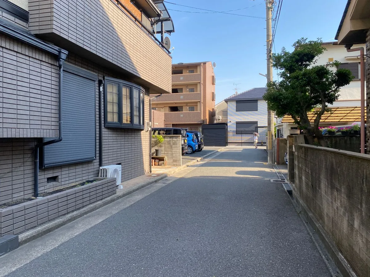 A narrow Japanese residential street lined with houses, low apartment blocks and parked kei cars.