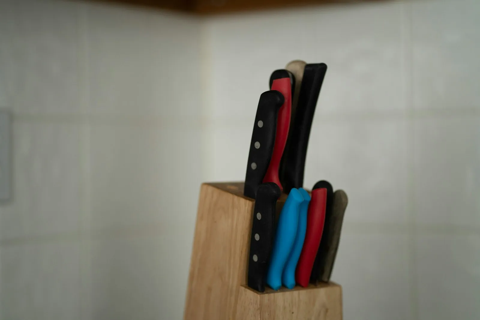 A wooden knife block holding several kitchen knives with coloured handles.