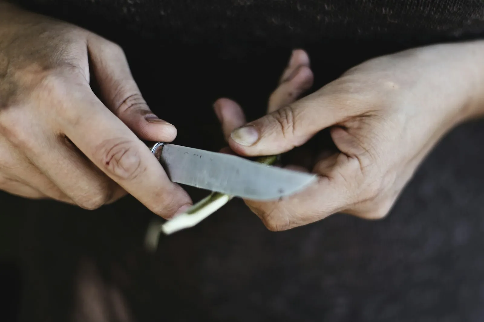 Two hands holding a kitchen knife blade over a dark surface.
