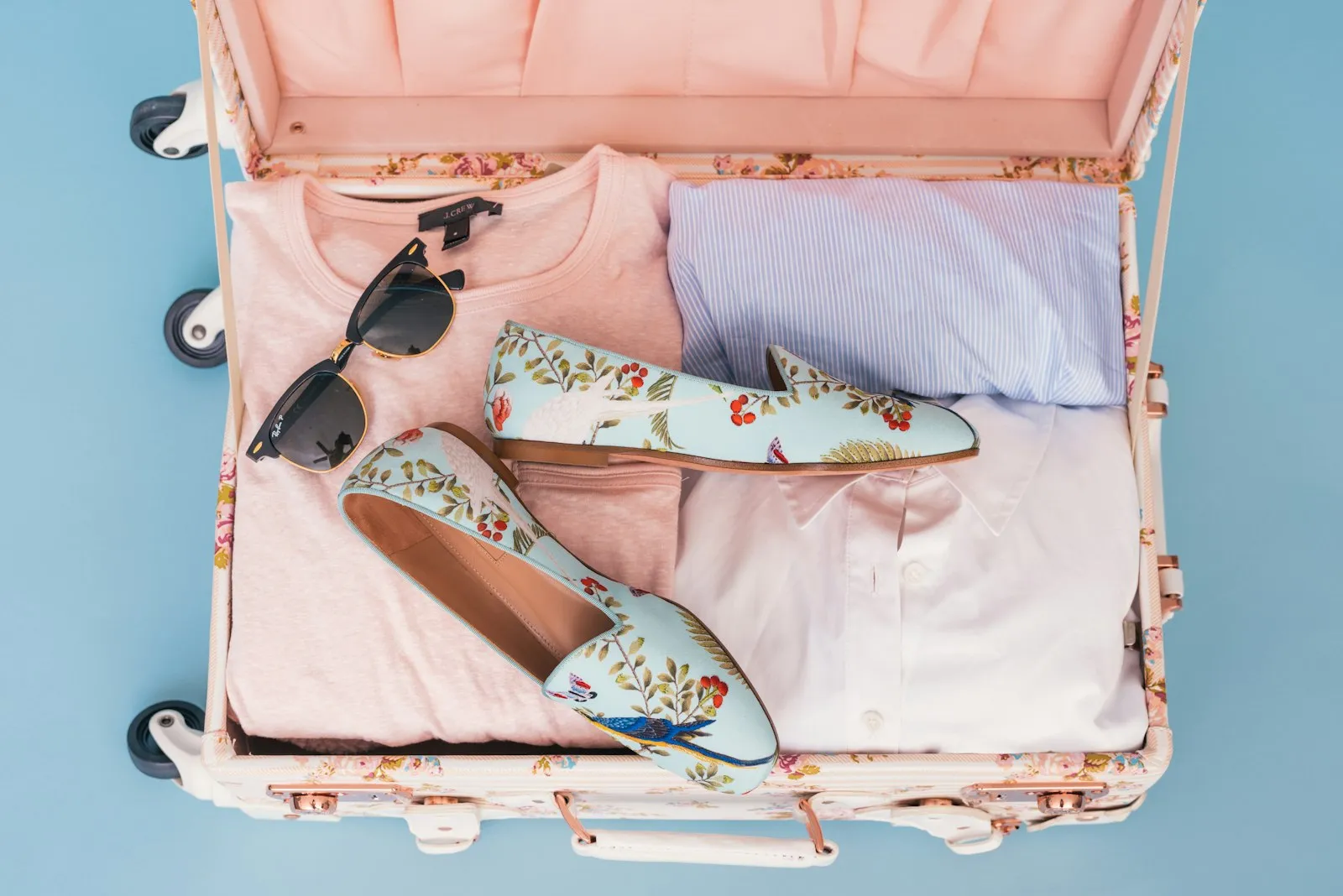 An open suitcase packed with folded clothes, shoes and sunglasses.